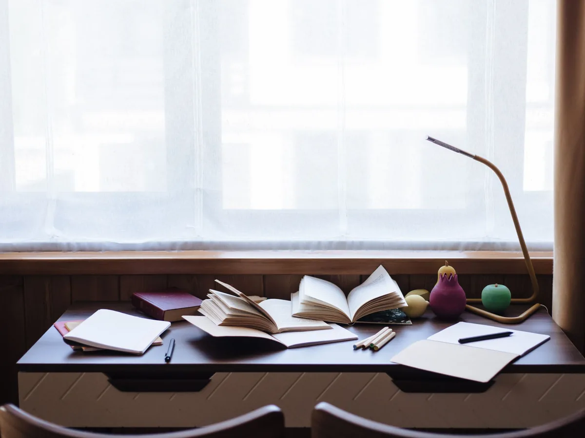 Un bureau de rédaction : carnets, journaux et une lampe, à la lumière du matin