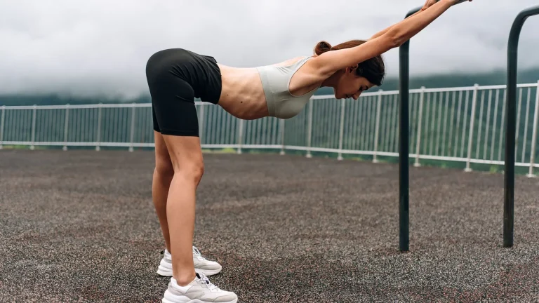 Femme qui s'étire les jambes en s'appuyant à une rambarde, en extérieur après l'effort
