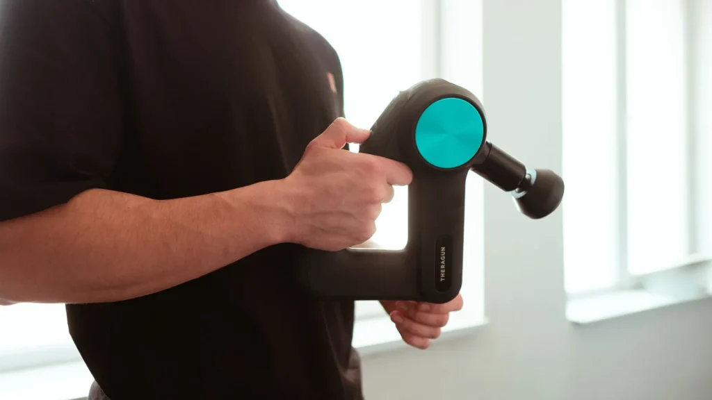 Homme tenant un pistolet de massage musculaire à côté d'une fenêtre