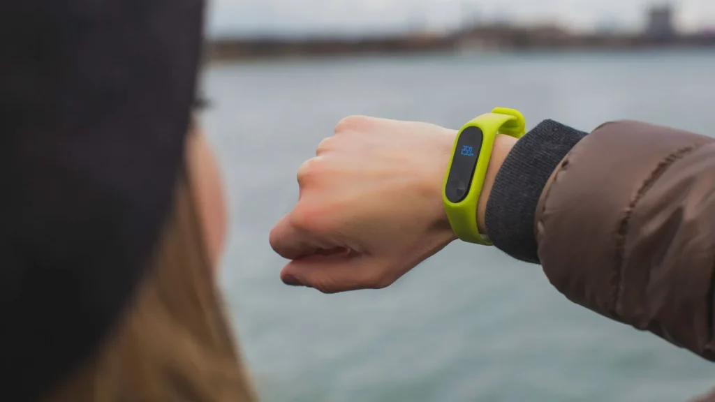 Poignet portant un bracelet connecté vert dont l'écran affiche une valeur