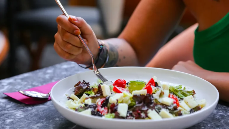 Main tenant une fourchette au-dessus d'un bol de salade, repas pris tranquillement à table