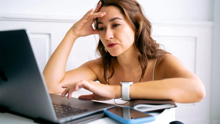 Femme stressée à son bureau, la main sur le front devant un ordinateur portable