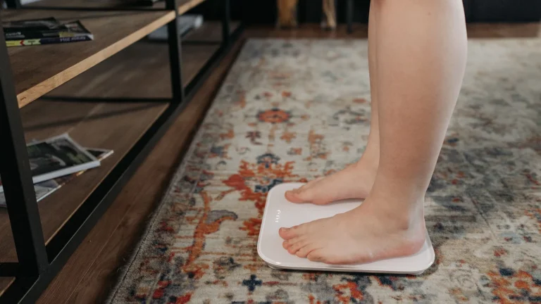 Femme debout pieds nus sur un pèse-personne blanc posé sur un tapis