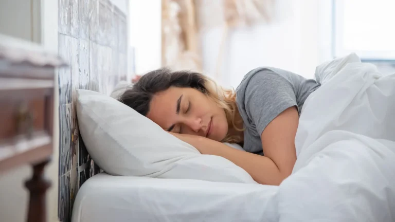Femme endormie sur le côté, la tête sur un oreiller, dans un lit aux draps blancs