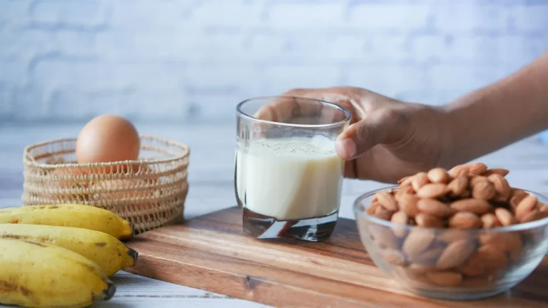 Verre de lait, bananes, œuf et bol d'amandes posés sur une planche en bois