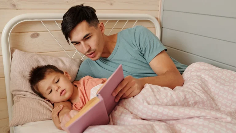 Père allongé près de son enfant dans un lit, lui lisant une histoire avant le coucher