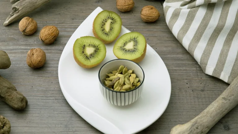 Kiwis coupés en deux, noix et petit bol de graines sur une assiette blanche