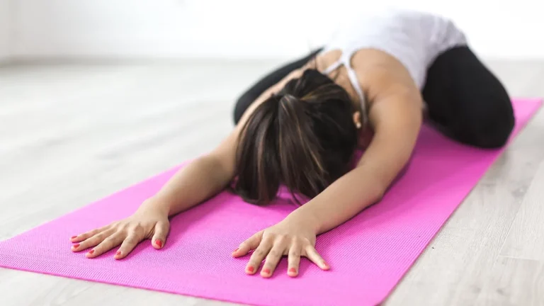 Femme en posture de l'enfant sur un tapis de yoga rose, étirement doux du dos