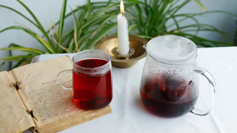Tasse et théière d'infusion rouge à côté d'une bougie allumée et d'un livre ouvert