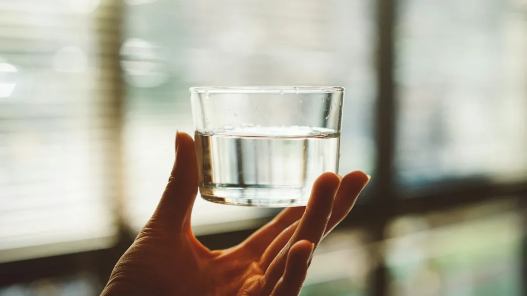 Main tenant un verre d'eau devant une fenêtre à stores