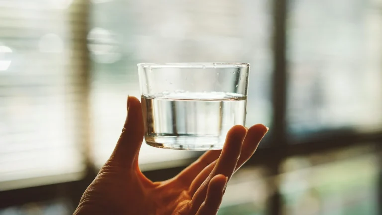 Main tenant un verre d'eau devant une fenêtre à stores