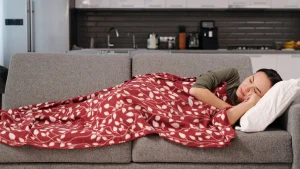 Femme endormie sur un canapé gris sous un plaid rouge pendant la sieste