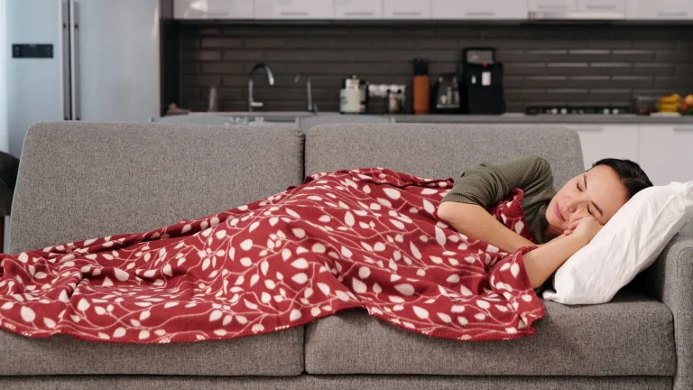 Femme endormie sur un canapé gris sous un plaid rouge pendant la sieste