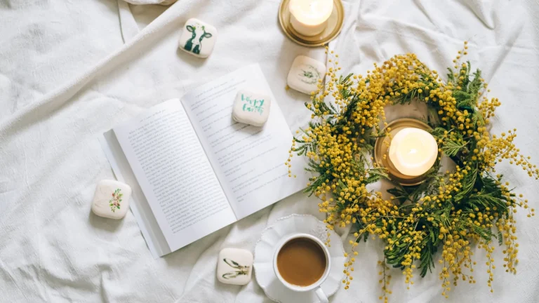 Livre ouvert, bougies et tasse posés sur un drap blanc pour un rituel de détente