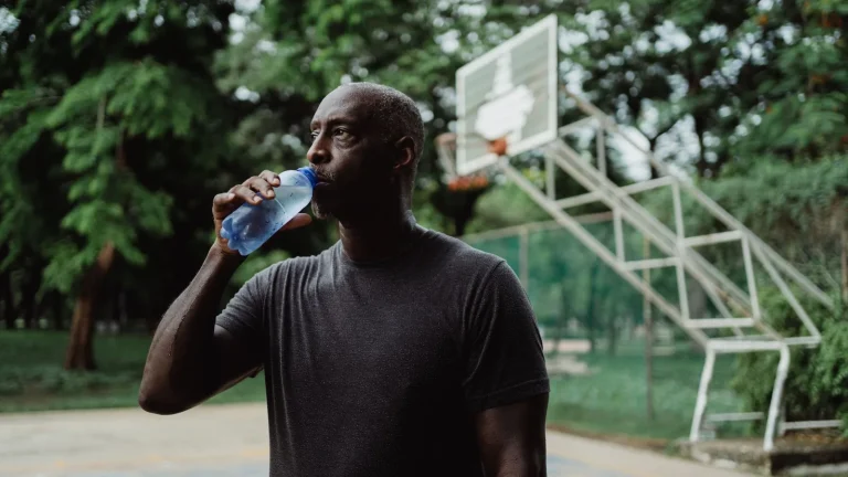 Sportif qui boit de l'eau à une bouteille sur un terrain de sport en plein air