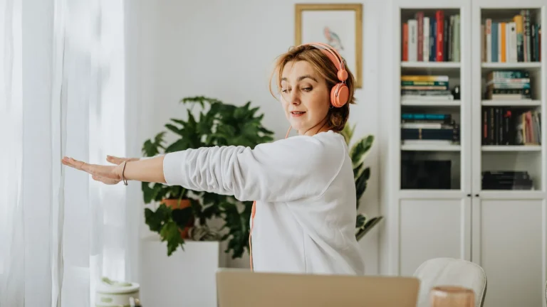 Femme qui s'étire bras tendus à côté de son bureau à domicile, casque sur les oreilles