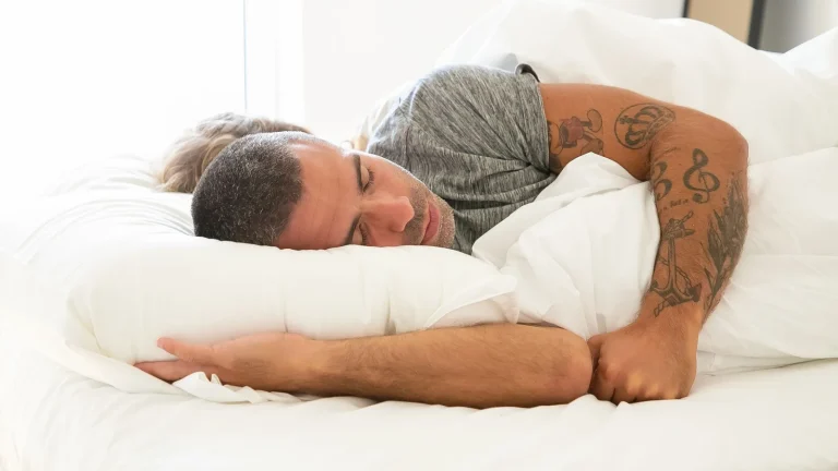 Homme qui dort paisiblement dans un lit blanc, serrant son oreiller