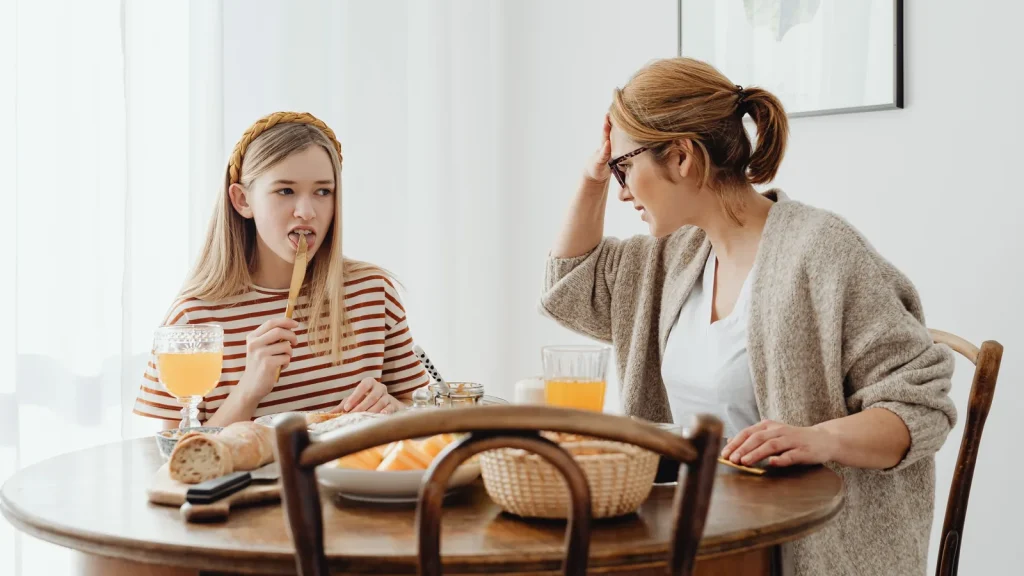 Adolescente à table pendant le repas, face à sa mère soucieuse, la main sur le front