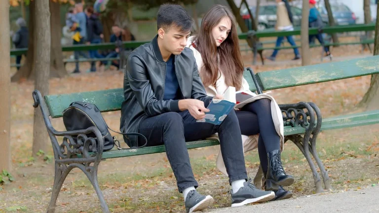 Deux jeunes assis sur un banc de parc qui consultent un livre