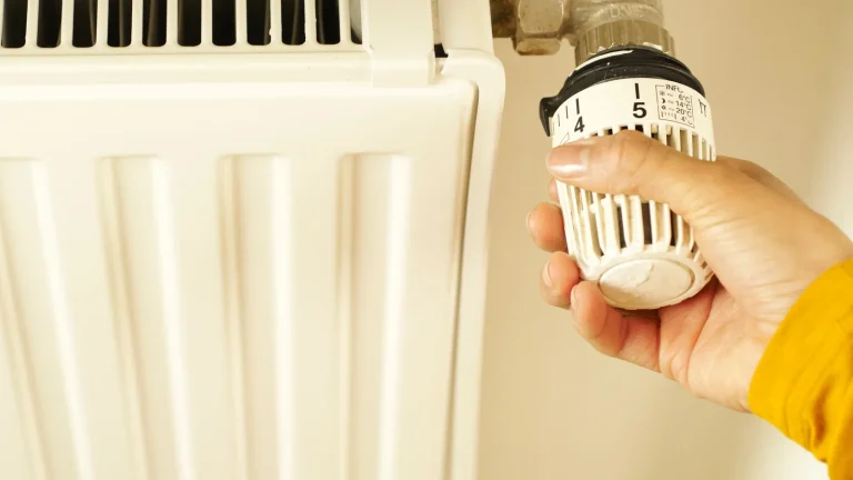 Main qui règle le robinet thermostatique d'un radiateur blanc