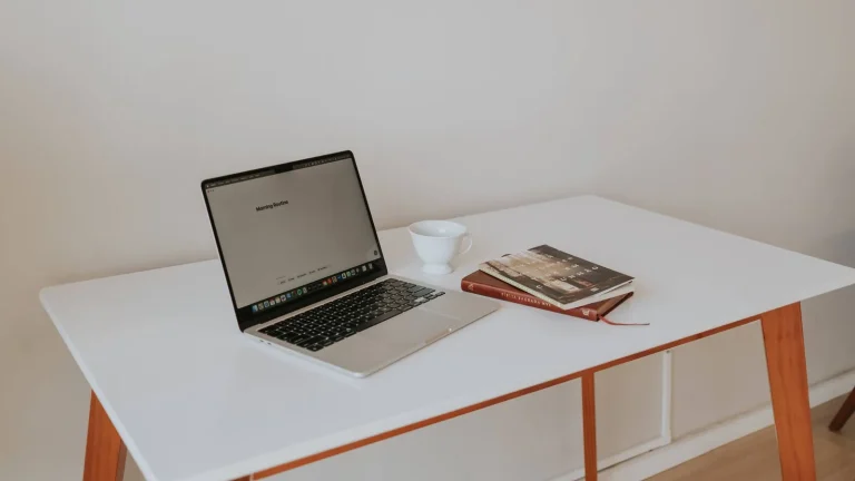 Poste de télétravail à la maison : ordinateur portable, tasse et livre sur un bureau blanc
