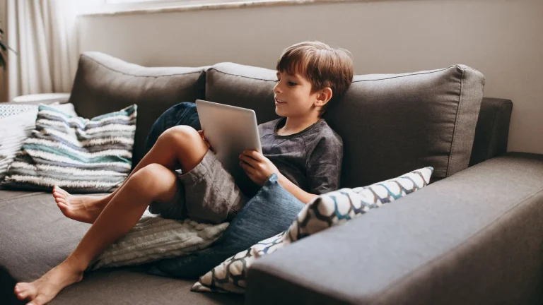 Enfant allongé sur un canapé avec une tablette numérique entre les mains