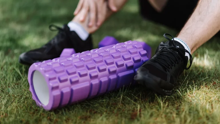 Rouleau de massage en mousse violet dans l'herbe, jambes d'un sportif assis